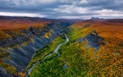 Elv som renner gjennom en dal omgitt av fargerik h&oslash;stnatur og fjell.