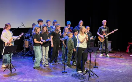 Kulturskolen på scenen Mange barn står på en scene, noen synger og noen spiller instrumenter