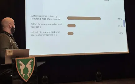En mann står og holder foredrag av en presentasjon i en sal.