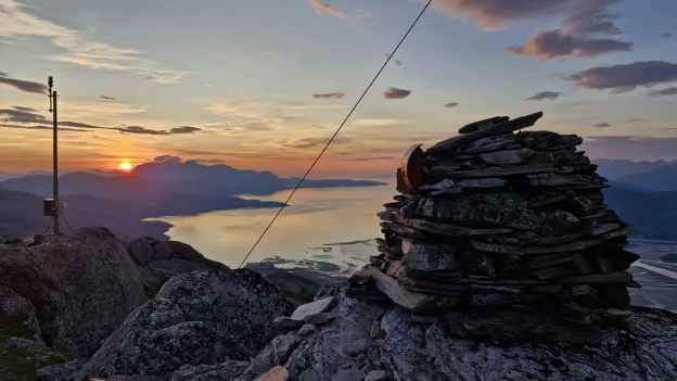 Solnedgang Solnedgang over fjord og fjell, sett fra en fjelltopp med en stor steinvarde i forgrunnen.