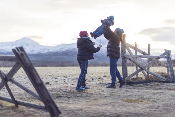 Samspill og glede i familien To voksne leker med et lite barn ute i et vinterlandskap.