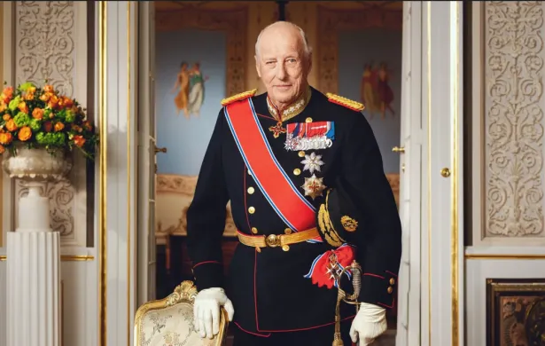 H. M Kong Harald V 1937-2026 Kong Harald står i gallauniform med ordener og medaljer i et rikt utsmykket rom på Slottet. Han holder en sabel i den ene hånden og støtter den andre på en stol.