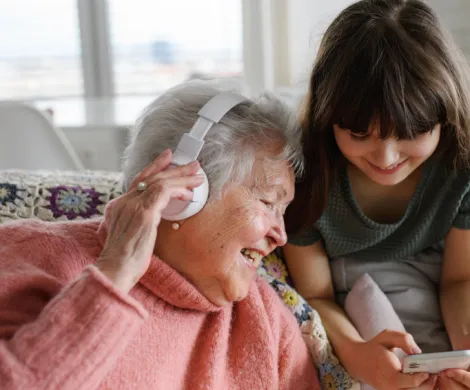 Eldre dame med ørehøytaler og et barn som viser en mobiltelefon til den eldre damen Eldre dame med ørehøytaler og et barn som viser en mobiltelefon til den eldre damen