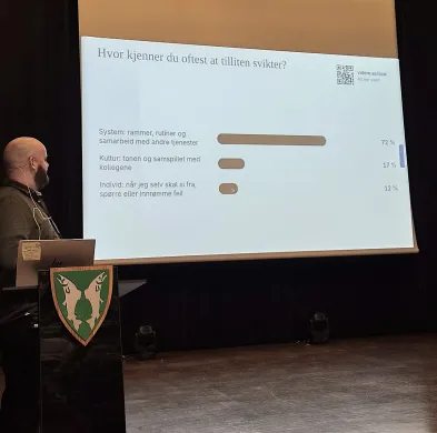 Foredrag En mann står og holder foredrag av en presentasjon i en sal.